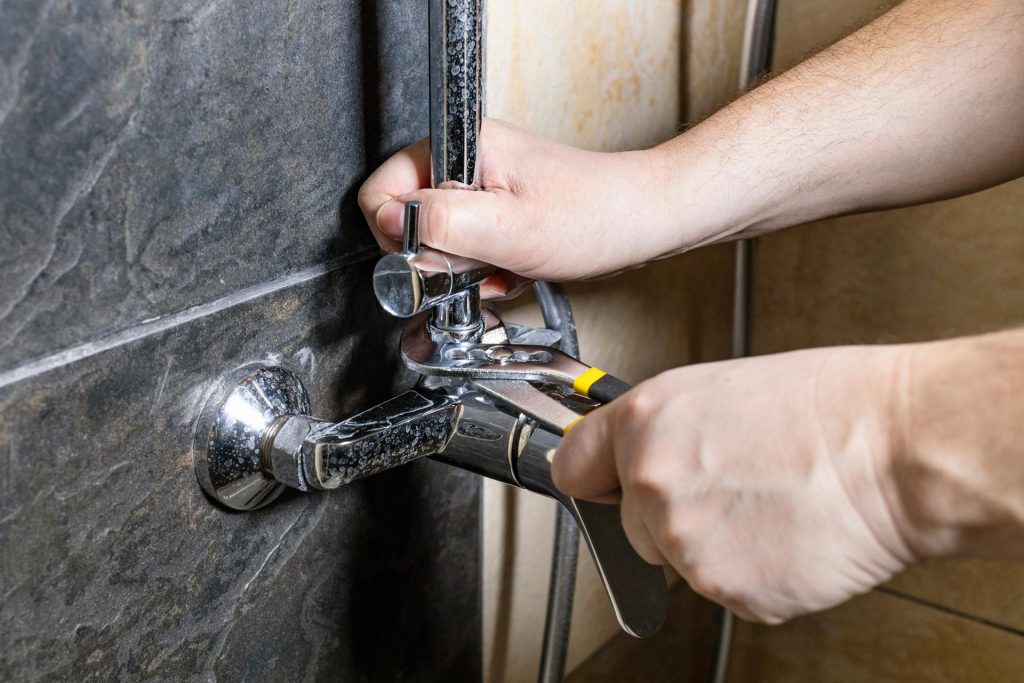 plumber fixes old shower faucet on tiled wall