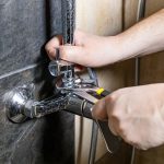 plumber fixes old shower faucet on tiled wall